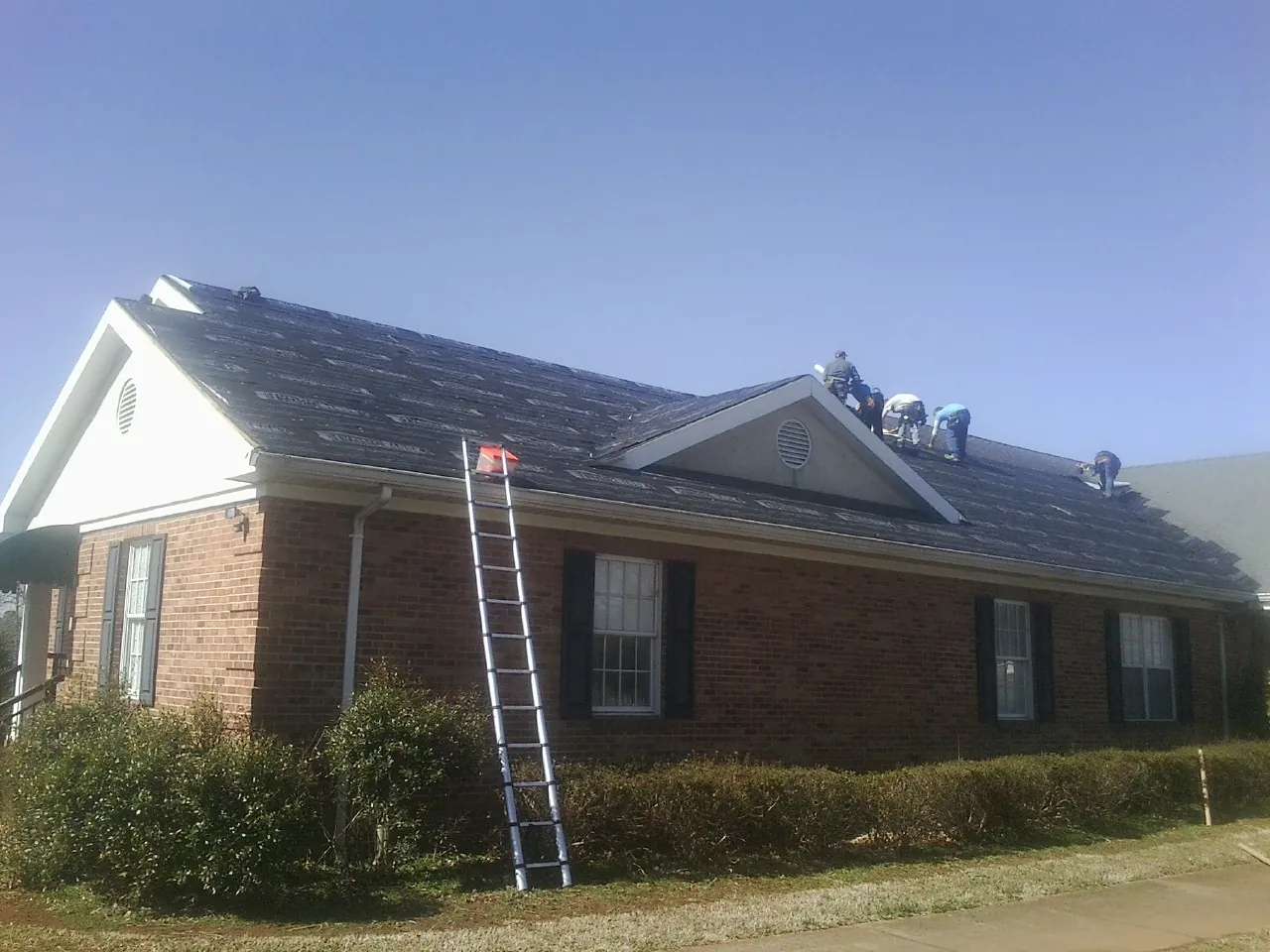 Crew tearing shingles off a brick ranch roof with a ladder set — Emergency Roof Repair work by our crew in Lagrange