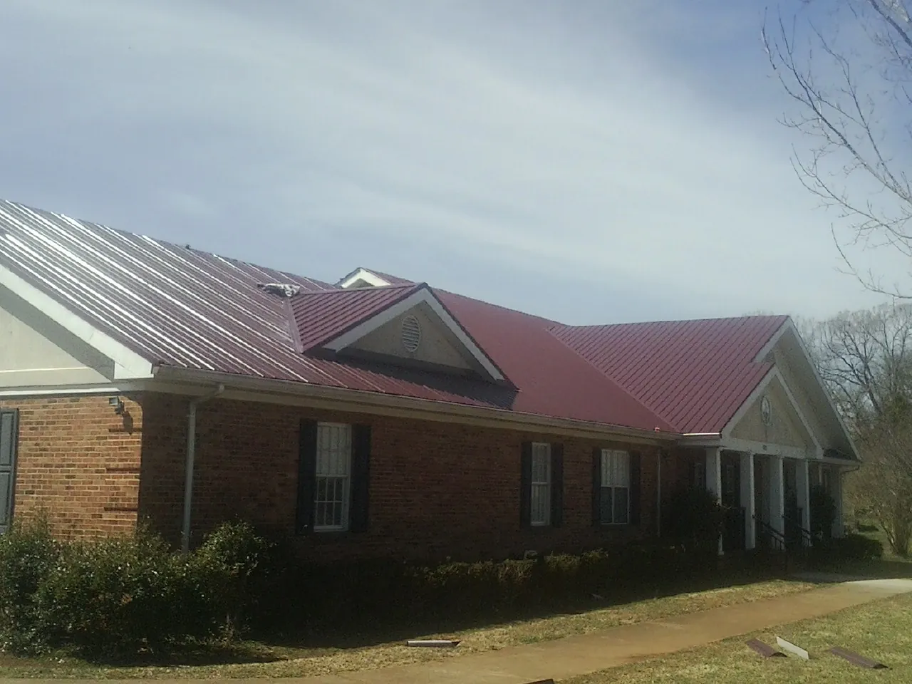 Red metal roof with gabled entries on a long brick building, from a Hail Damage Roof Repair job in Lagrange