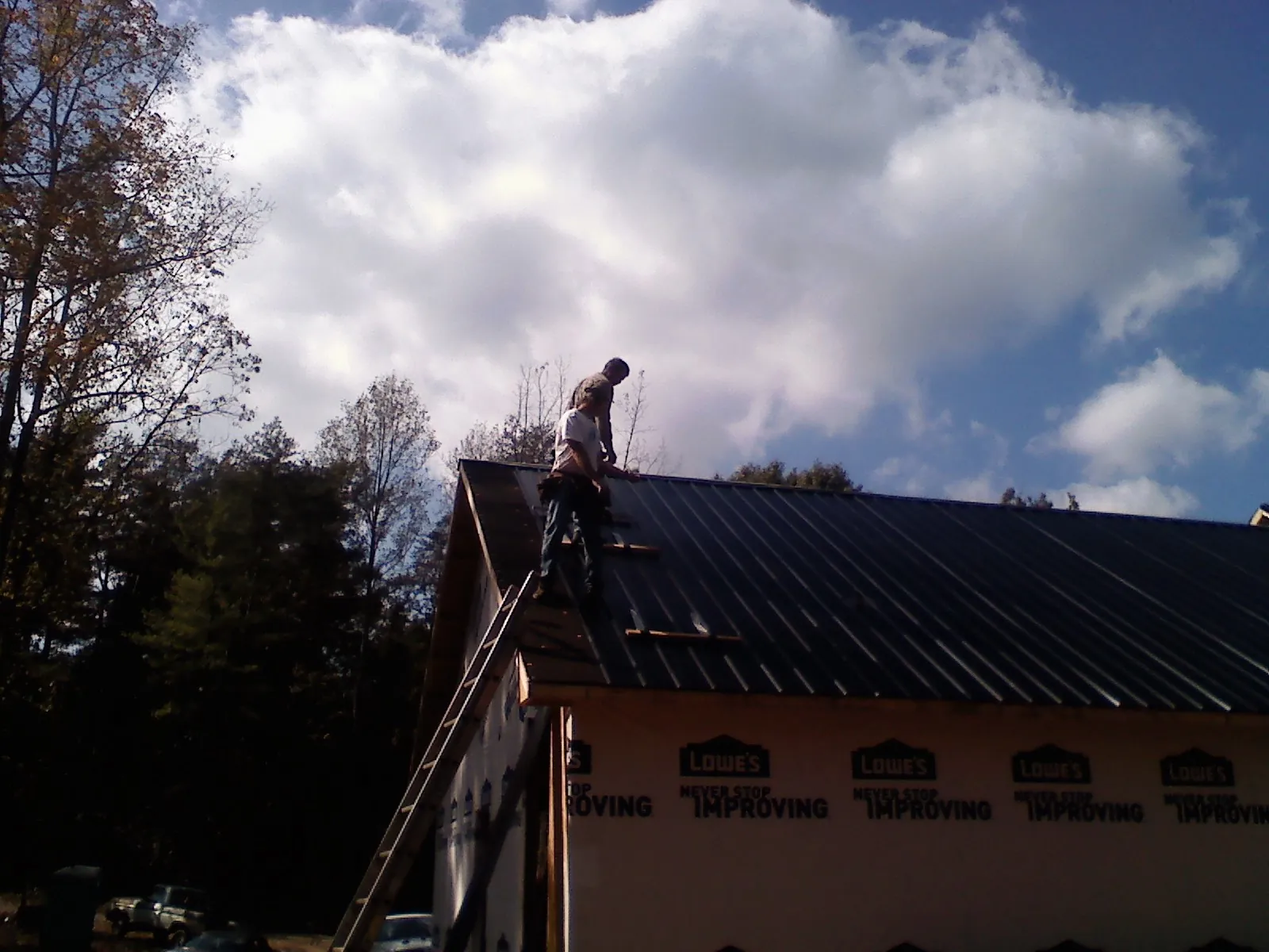 Roofer fastening dark metal panels high against a cloudy sky, from a Roof Inspection job in Lagrange